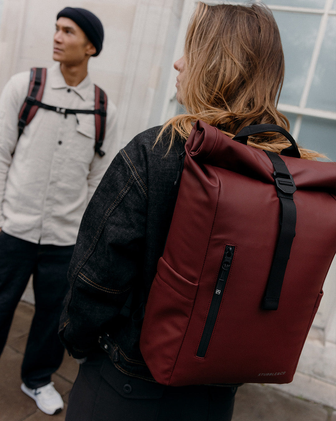 A man and woman wearing Roll Top 15l and 20l on their backs with the chest straps done up and a close up of the back on the womans bag showing the roll