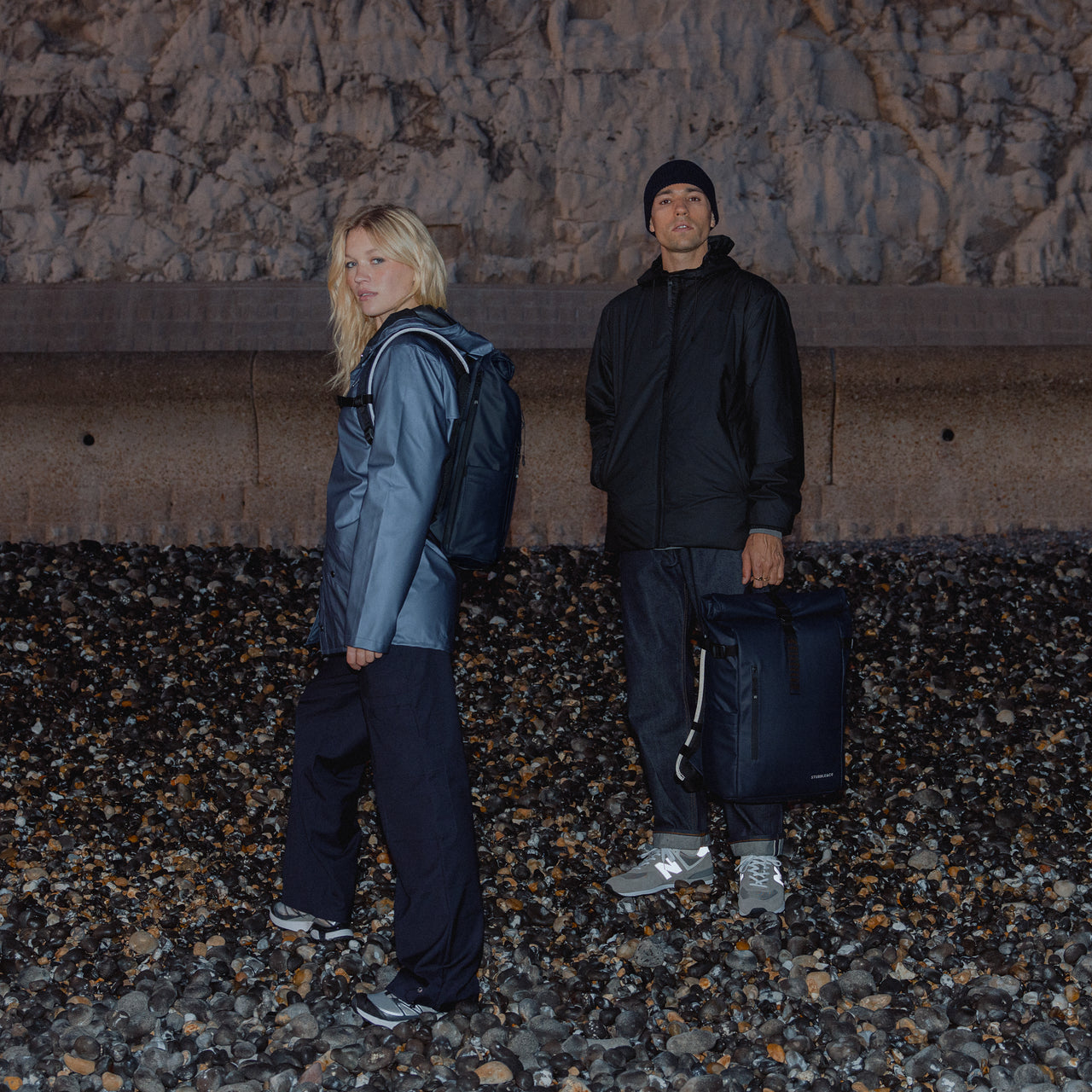 A man wearing a Roll Top 15L in Midnight Blue on her back and a man holding a Roll Top 20L by his side