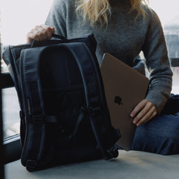 A woman placing a laptop into the laptop compartment in a Roll Top 15L in Midnight Blue