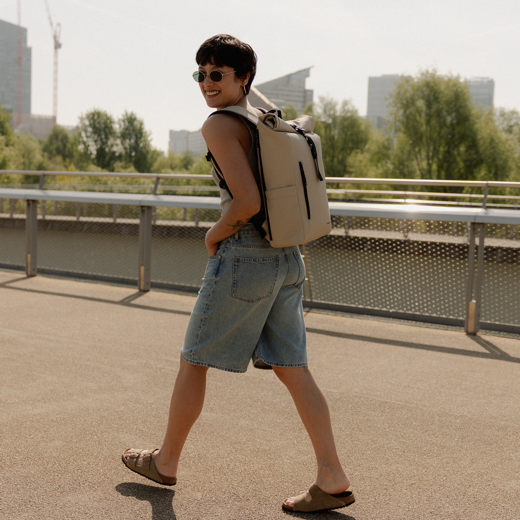 A woman walking away showing the side profile of the Sand roll top 15l on her back