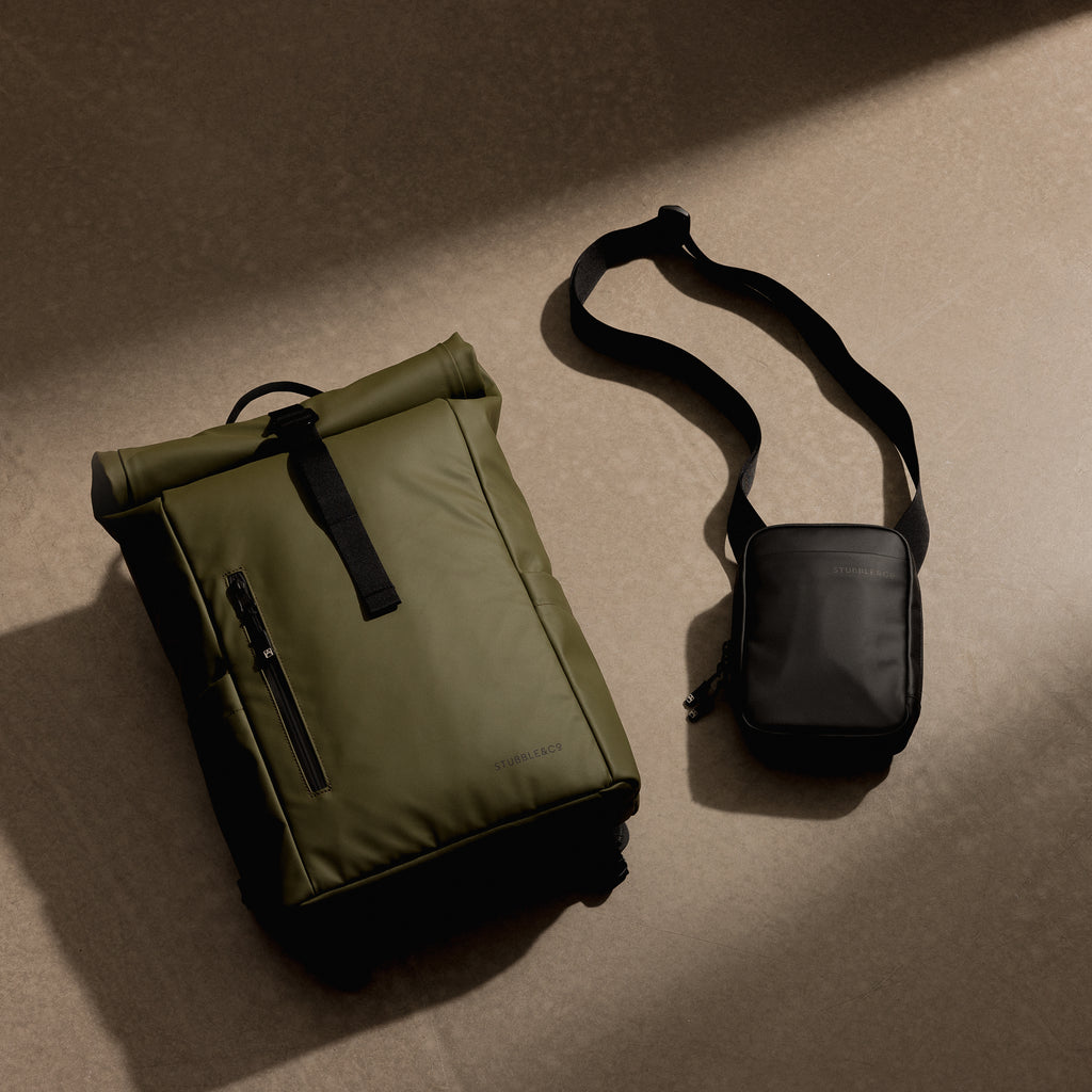 A studio shot of a green roll top 15l and a black shoulder bag on the floor as a creative flat lay