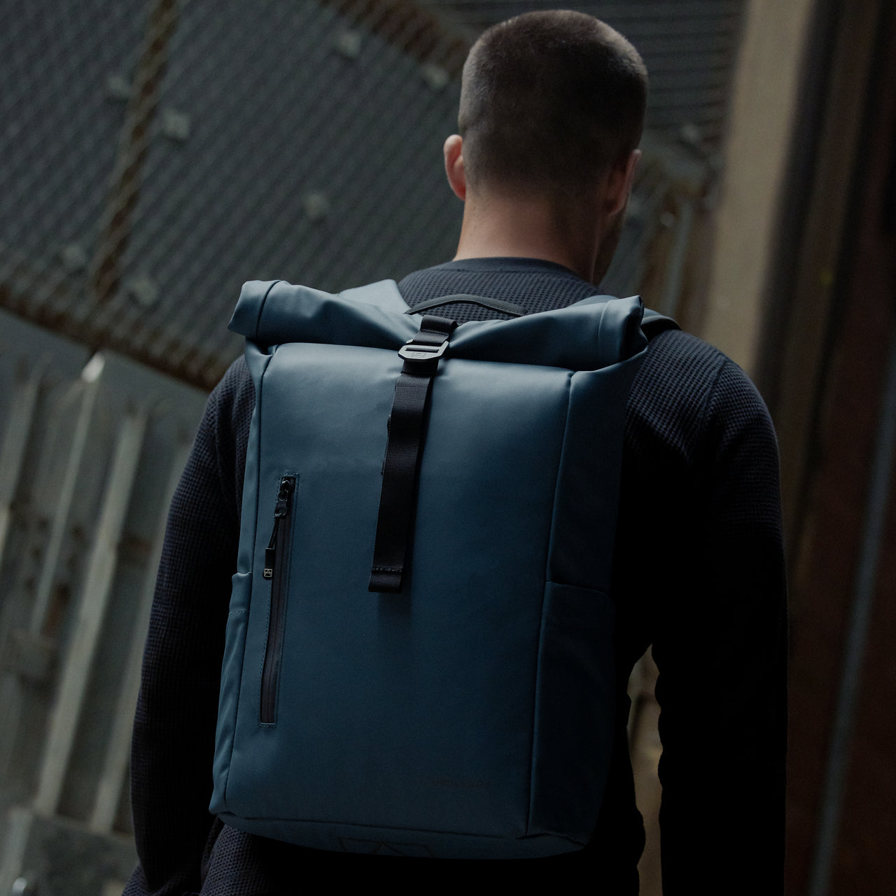 A man walking with a Roll Top 15L backpack in Tasmin Blue on his back