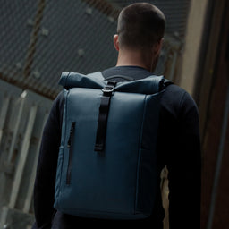 A man walking with a Roll Top 15L backpack in Tasmin Blue on his back