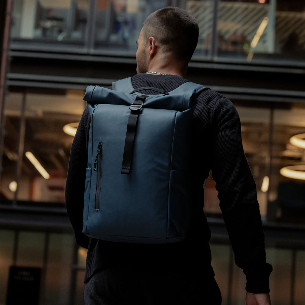A man wearing a Roll Top 15L backpack on his back in Tasmin Blue