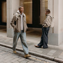 A man and woman standing on a pavement wearing Roll Top backpacks on their backs in Tonal Sand