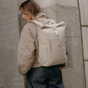A woman facing away wearing a Roll Top 15L on her back in Tonal Sand