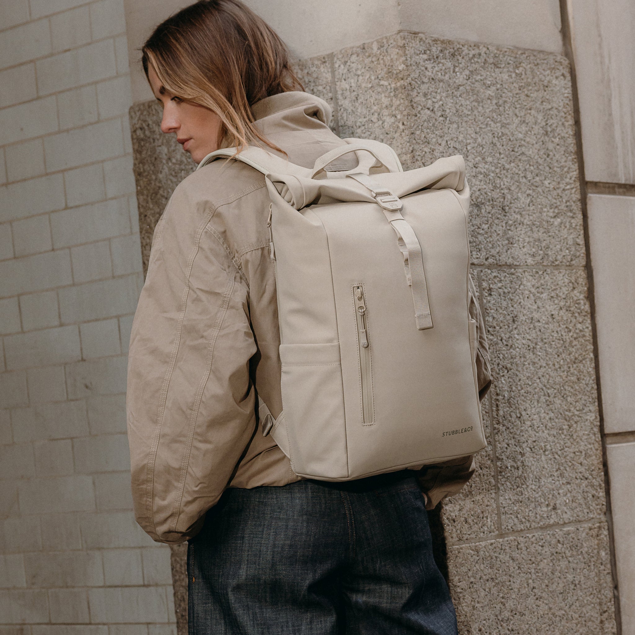 A woman facing away wearing a Roll Top 15L on her back in Tonal Sand