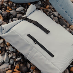 The Roll Top 15L in Arctic White on a pebble beach