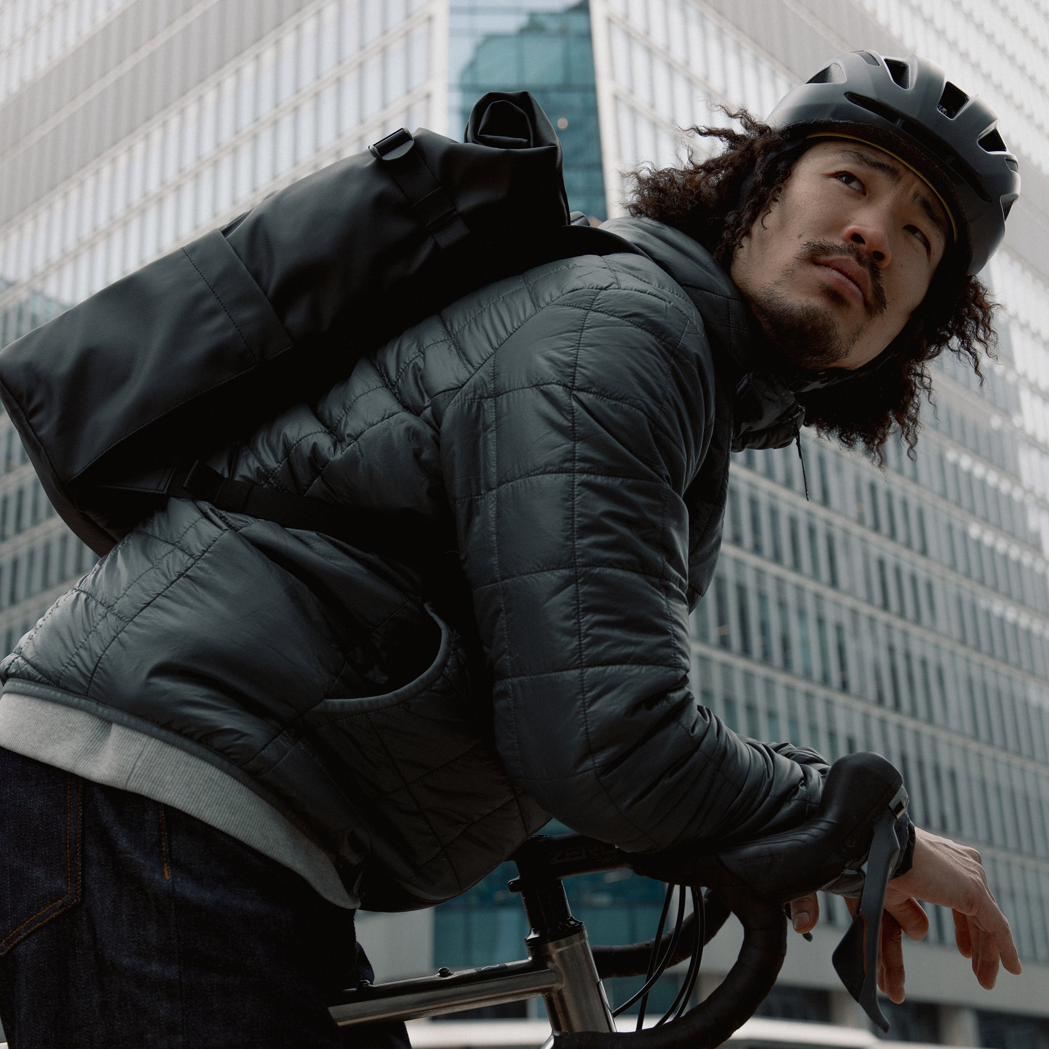 Man wearing The Roll Top 20L Backpack in All Black on a bike