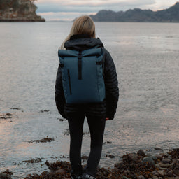 Women wearing The Roll Top 20L backpack in Tasmin Blue by water