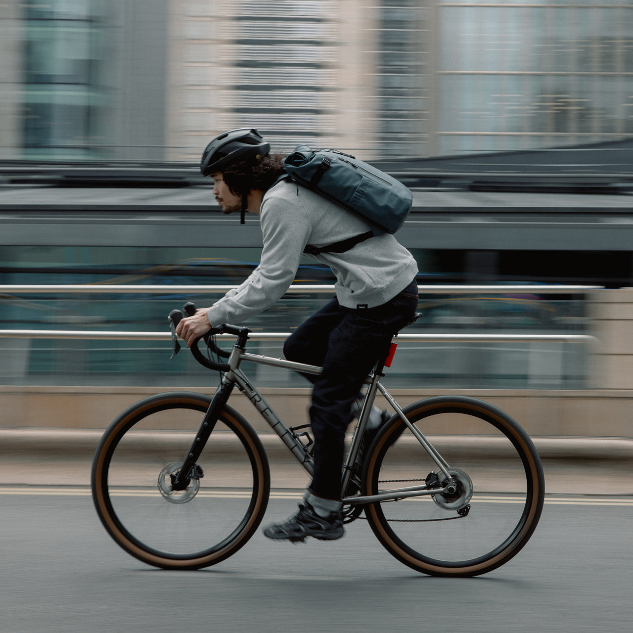 Man wearing The Roll Top 20L backpack in Tasmin Blue on a bike