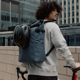 Man wearing The Roll Top 20L backpack in Tasmin Blue on a bike