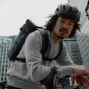 Man wearing The Roll Top 20L backpack in Tasmin Blue on a bike with a helmet on his head