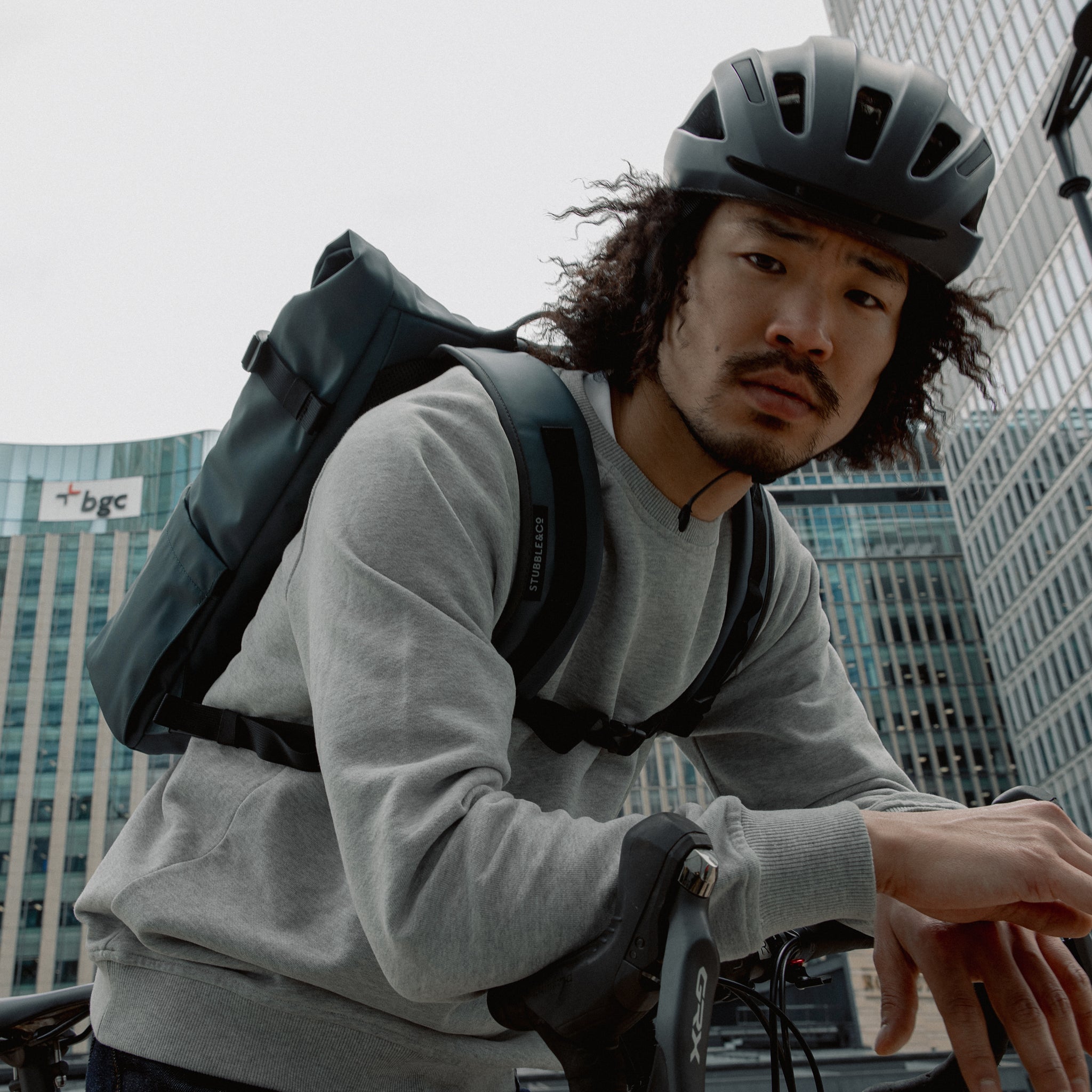 Man wearing The Roll Top 20L backpack in Tasmin Blue on a bike with a helmet on his head