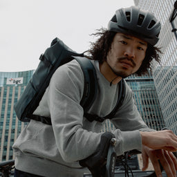 Man wearing The Roll Top 20L backpack in Tasmin Blue on a bike with a helmet on his head