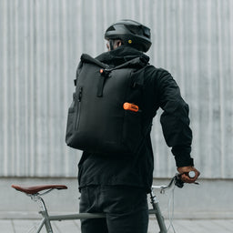 Cyclist in a helmet with a bike, wearing The Roll Top 20L in All Black