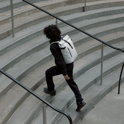 Man wearing The Roll Top 20L in Arctic White running up steps