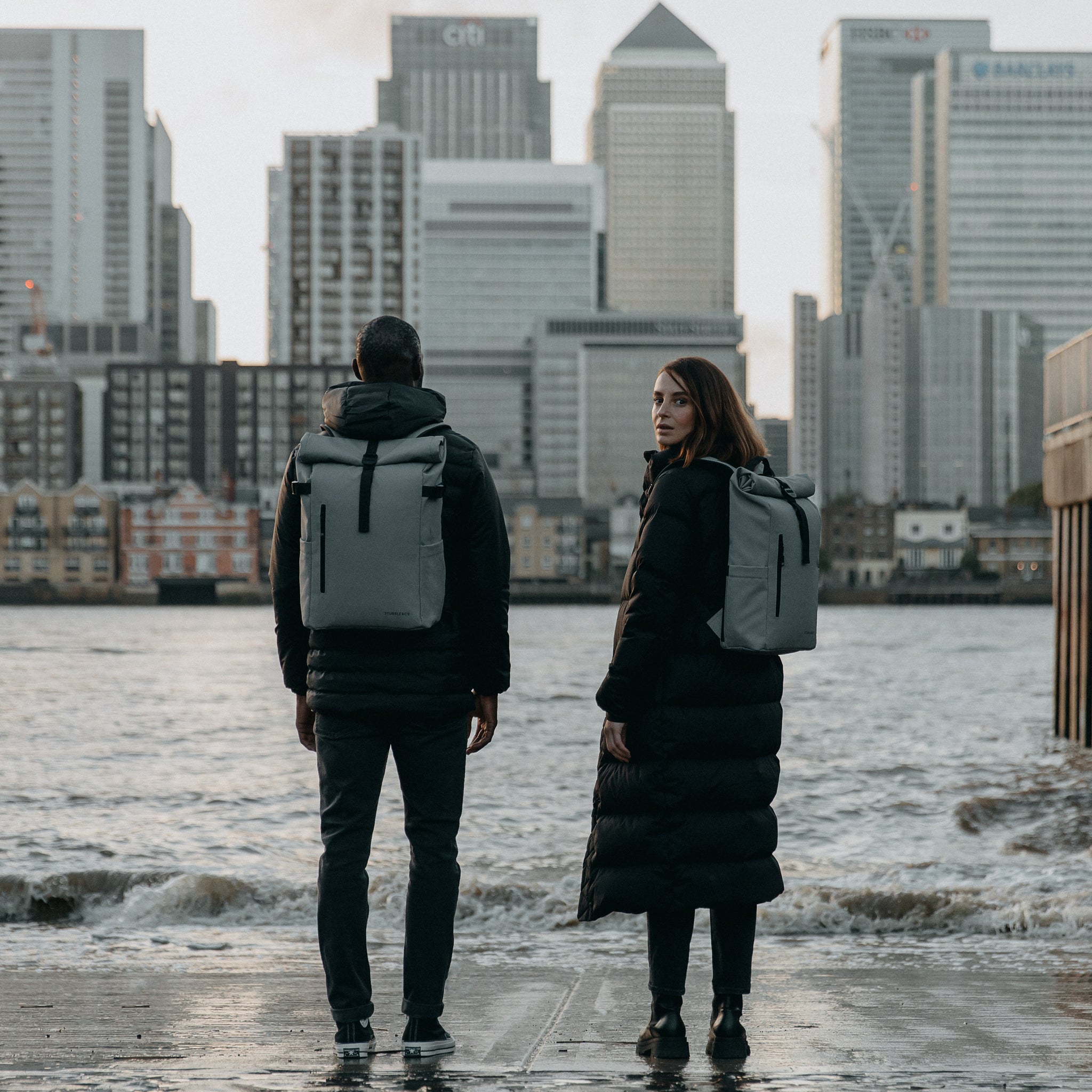 Man and women wearing the Roll Top 15L in Concrete standing by the edge of a river in a city