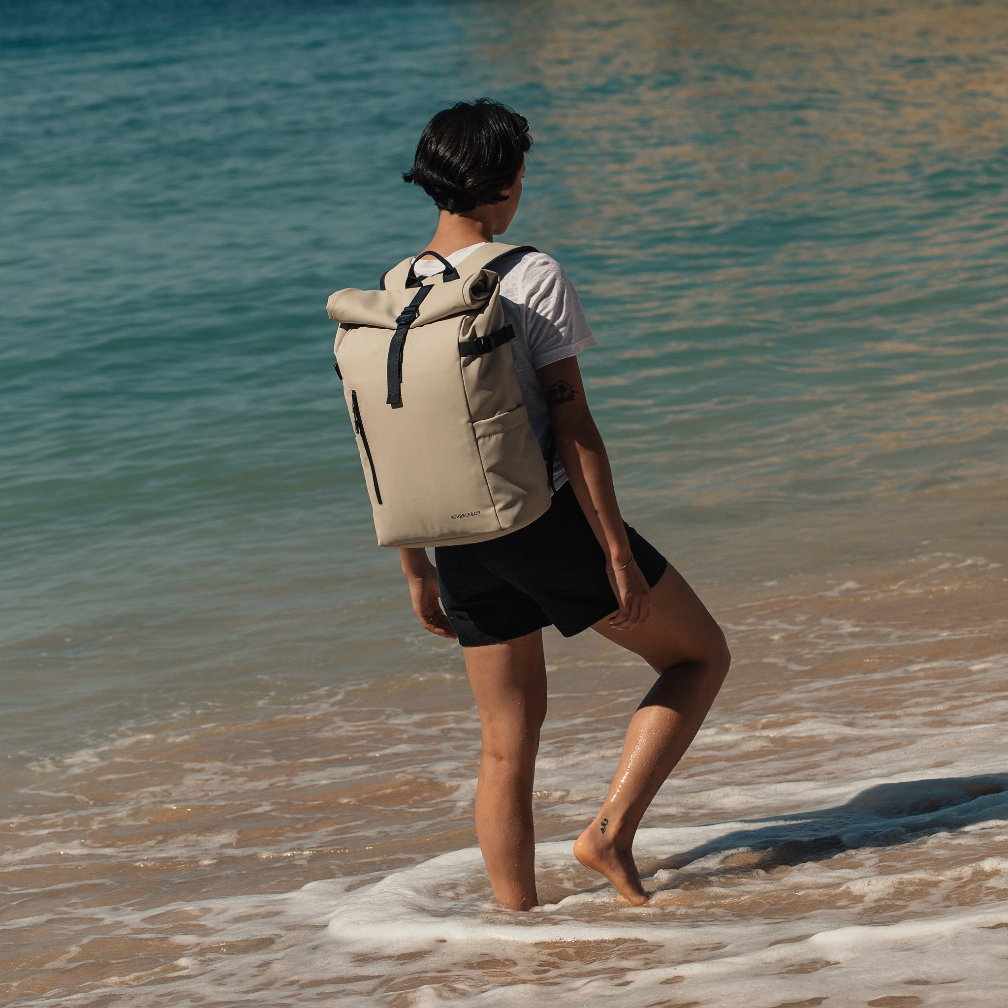 Women wearing The Roll Top 20L backpack in Sand paddling in the sea