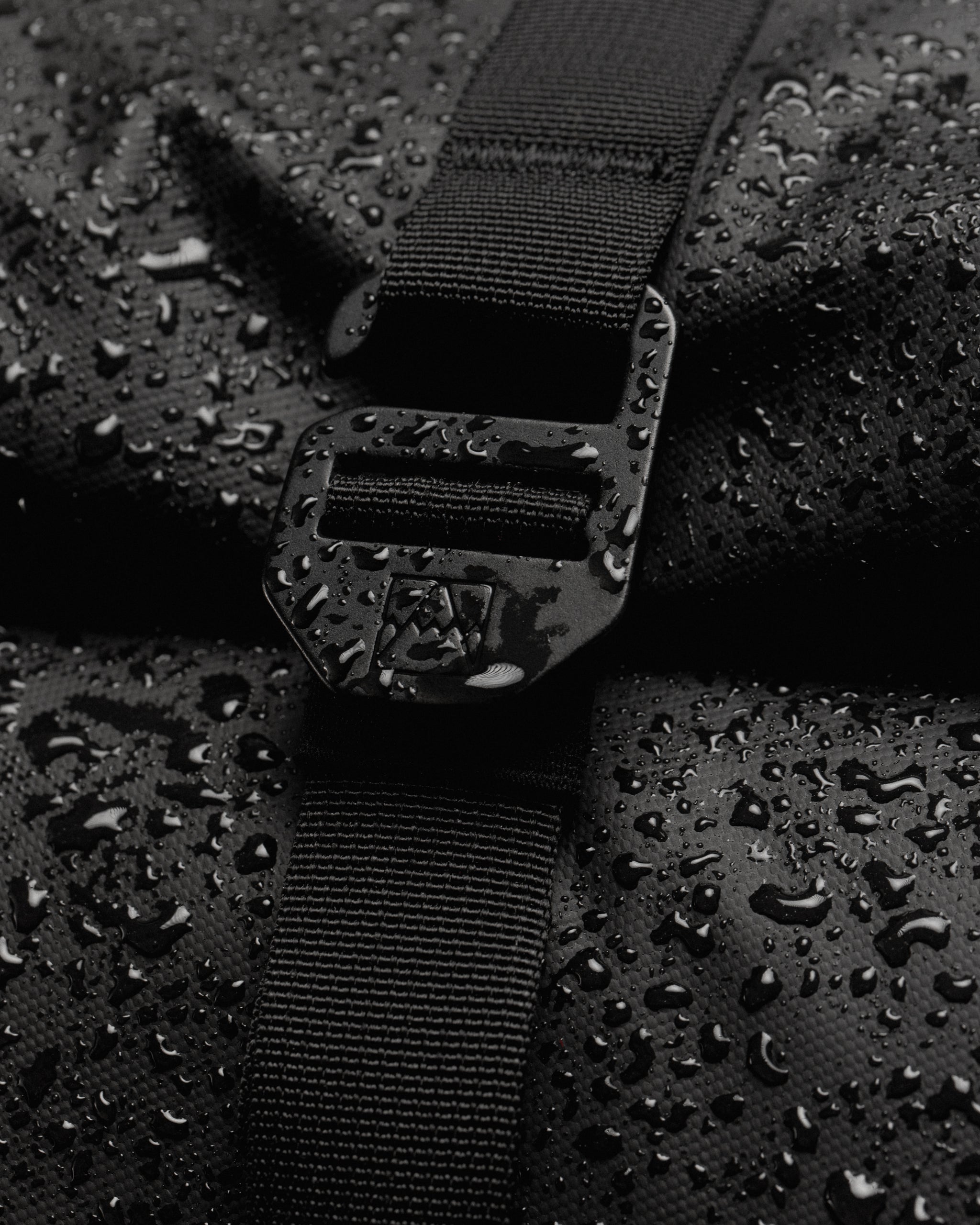 Close up of Roll Top backpack G-hook fastening with rain droplets on the bag