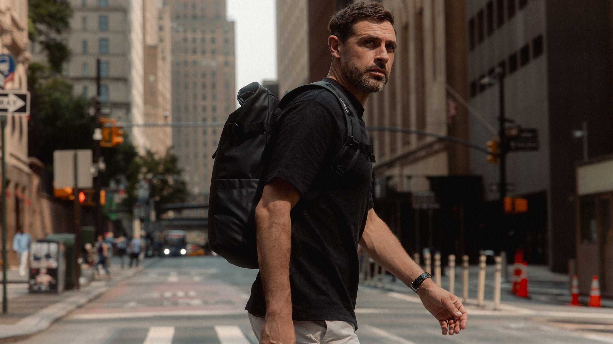 A man crossing the street in new york wearing a roll top 20l on his back