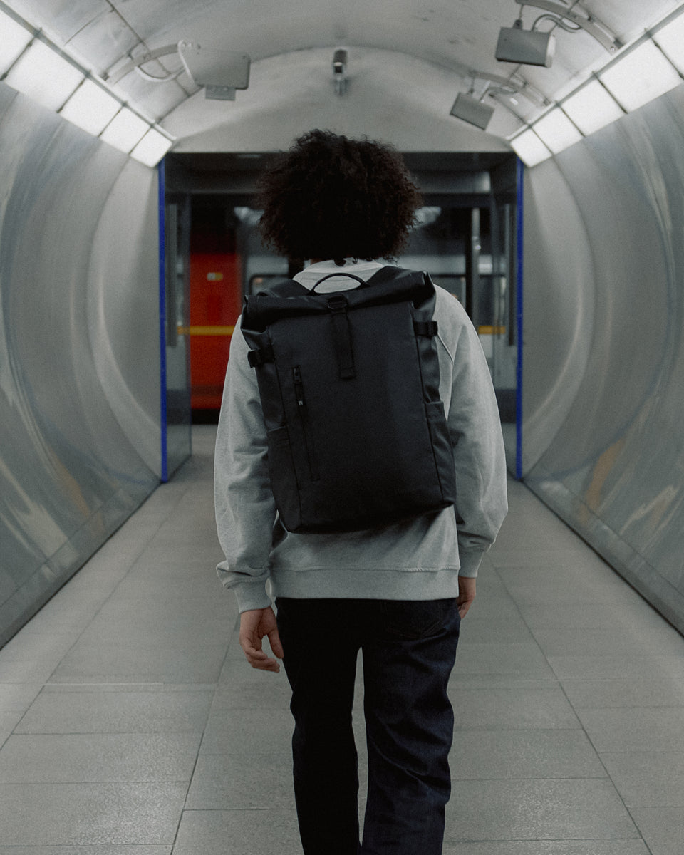 a man walking towards the tube wearing an all black 20l roll top on his back