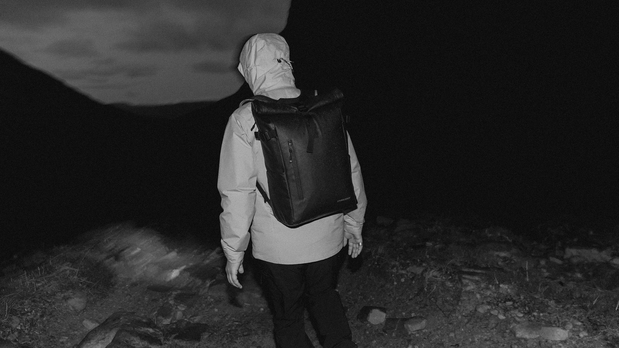a black and white shot of a man on a hike wearing a roll top 20l on his back