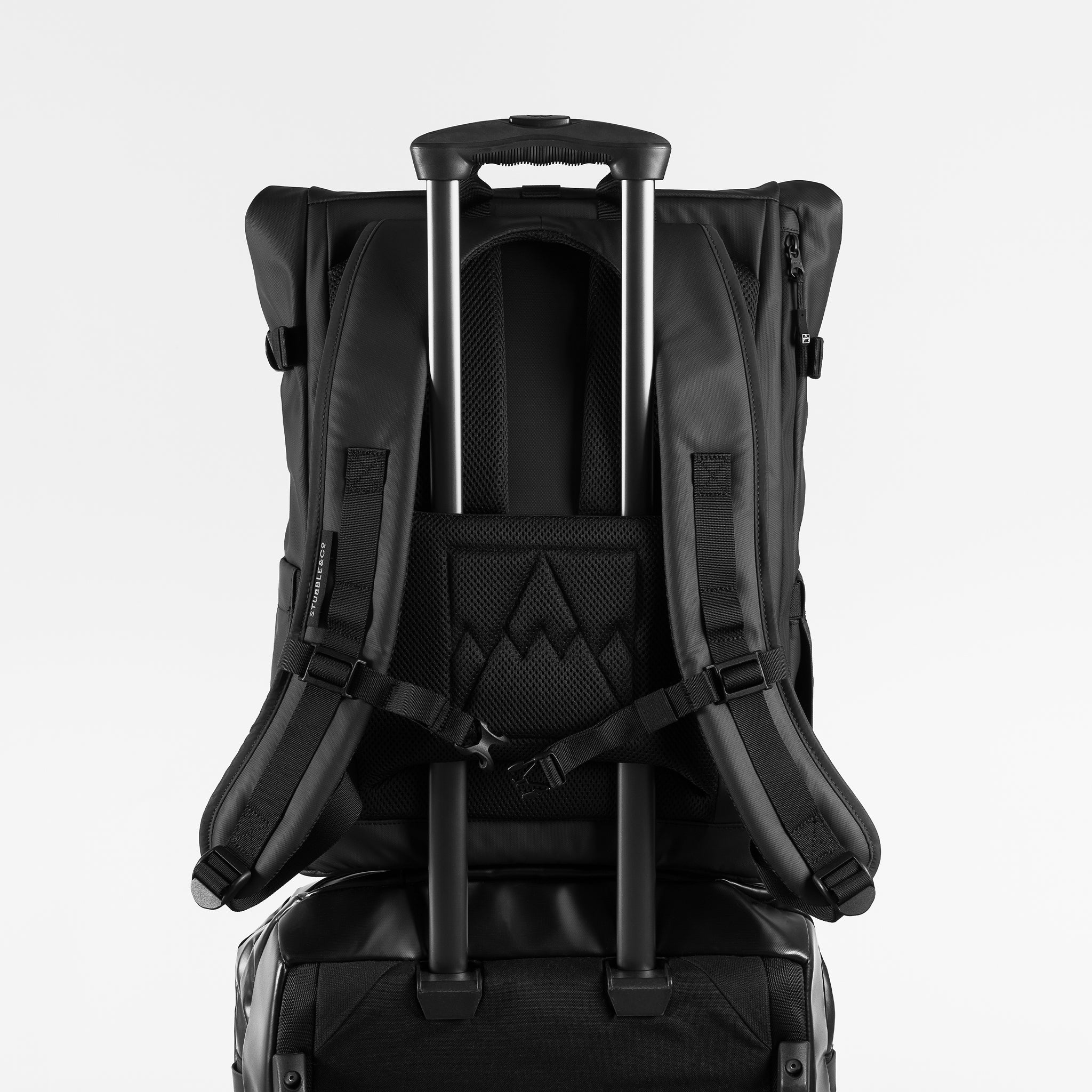 A studio shot of the luggage sleeve in use on an All Black Roll Top 20L backpack