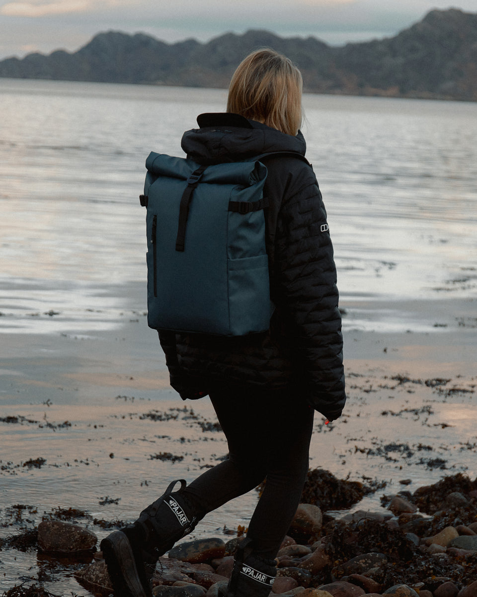 A woman standing next to a lake wearing a tasmin blue roll top 20l on her back