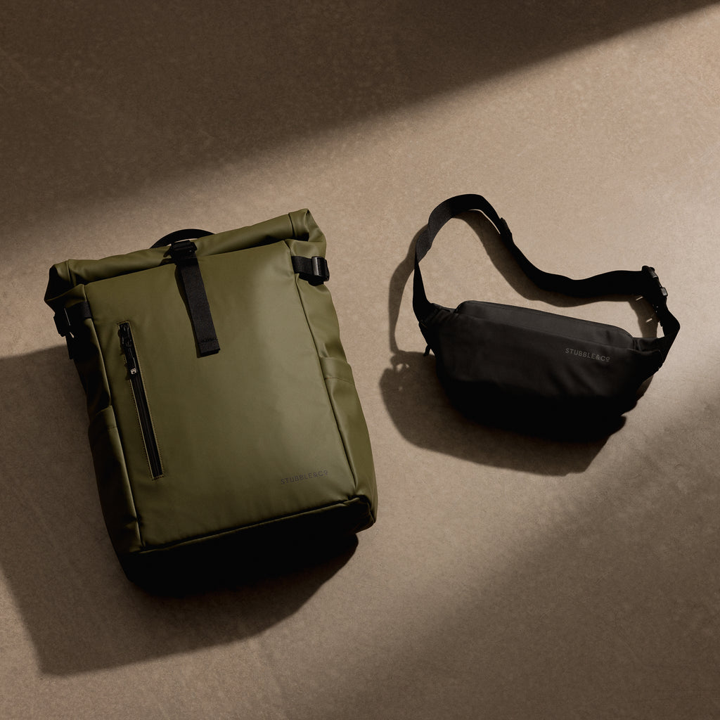 A studio shot of a green roll top 20l and black crossbody on the floor as a creative flat lay