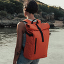 Women wearing The Roll Top 20L backpack in Ember Orange on a beach