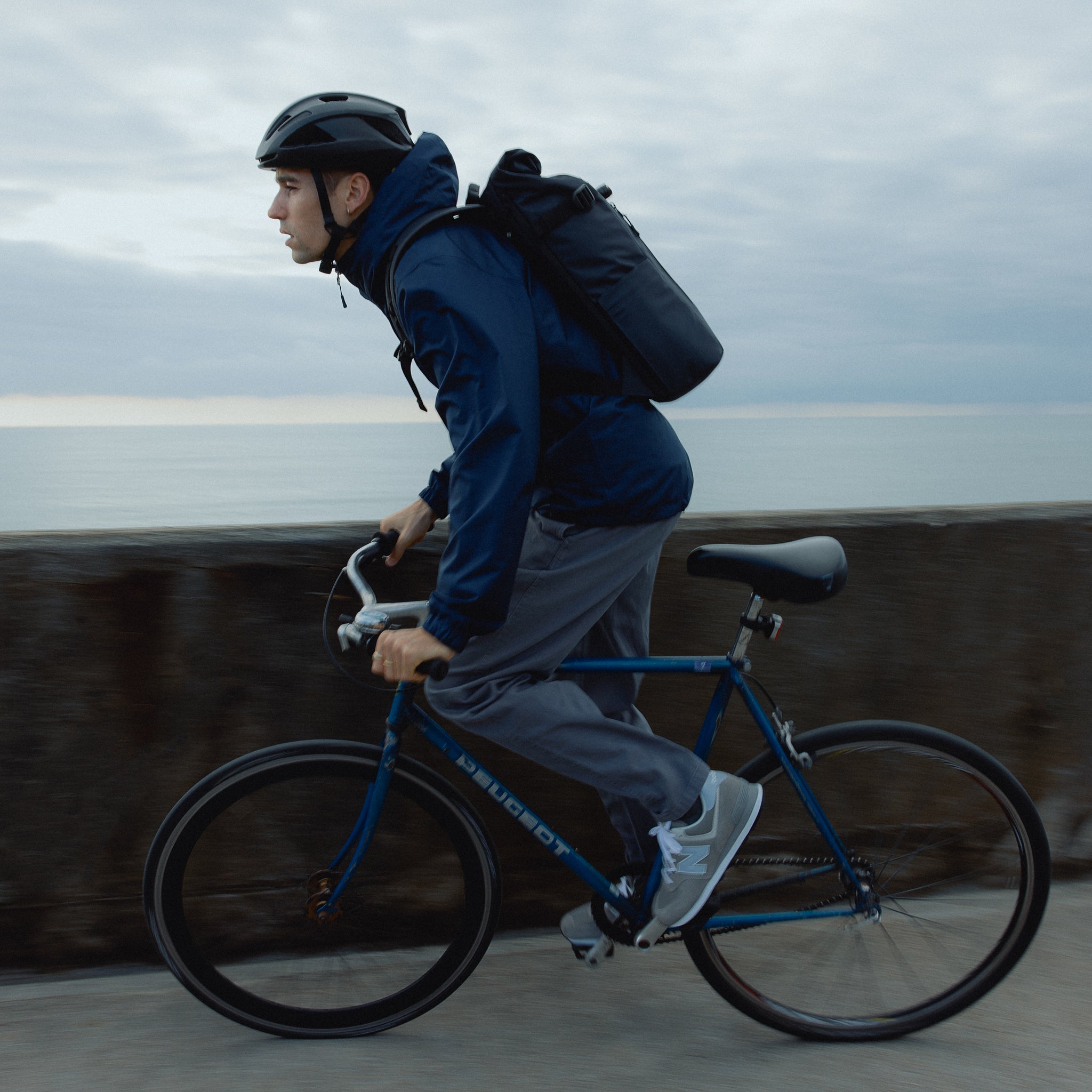 A man cycling a bike wearing a Roll Top 20L in Midnight Blue on his back