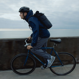 A man cycling a bike wearing a Roll Top 20L in Midnight Blue on his back