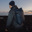 A man wearing a Roll Top 20L in Midnight Blue on his back with the sunset in the background
