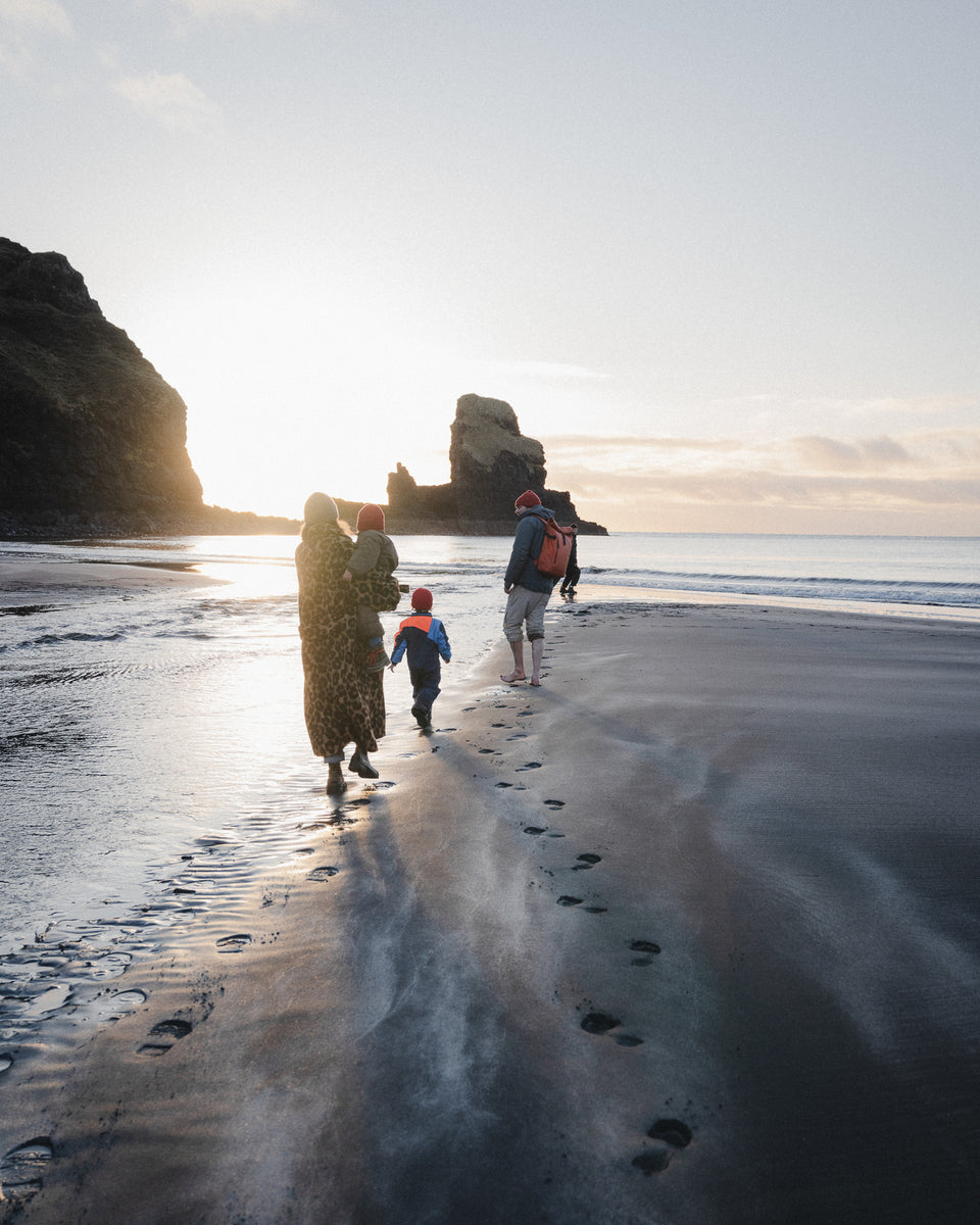a family on the beach and the man wearing a roll top 20l in rust
