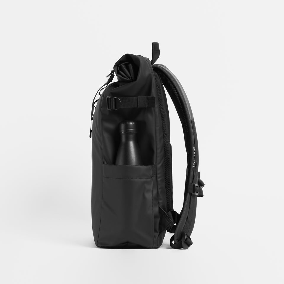 Product shot side view of The Roll Top 20L in All Black with a water bottle in the side pocket.