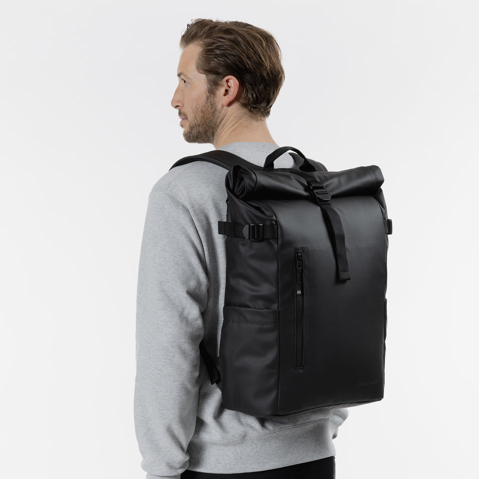 Man wearing The Roll Top 20L black backpack