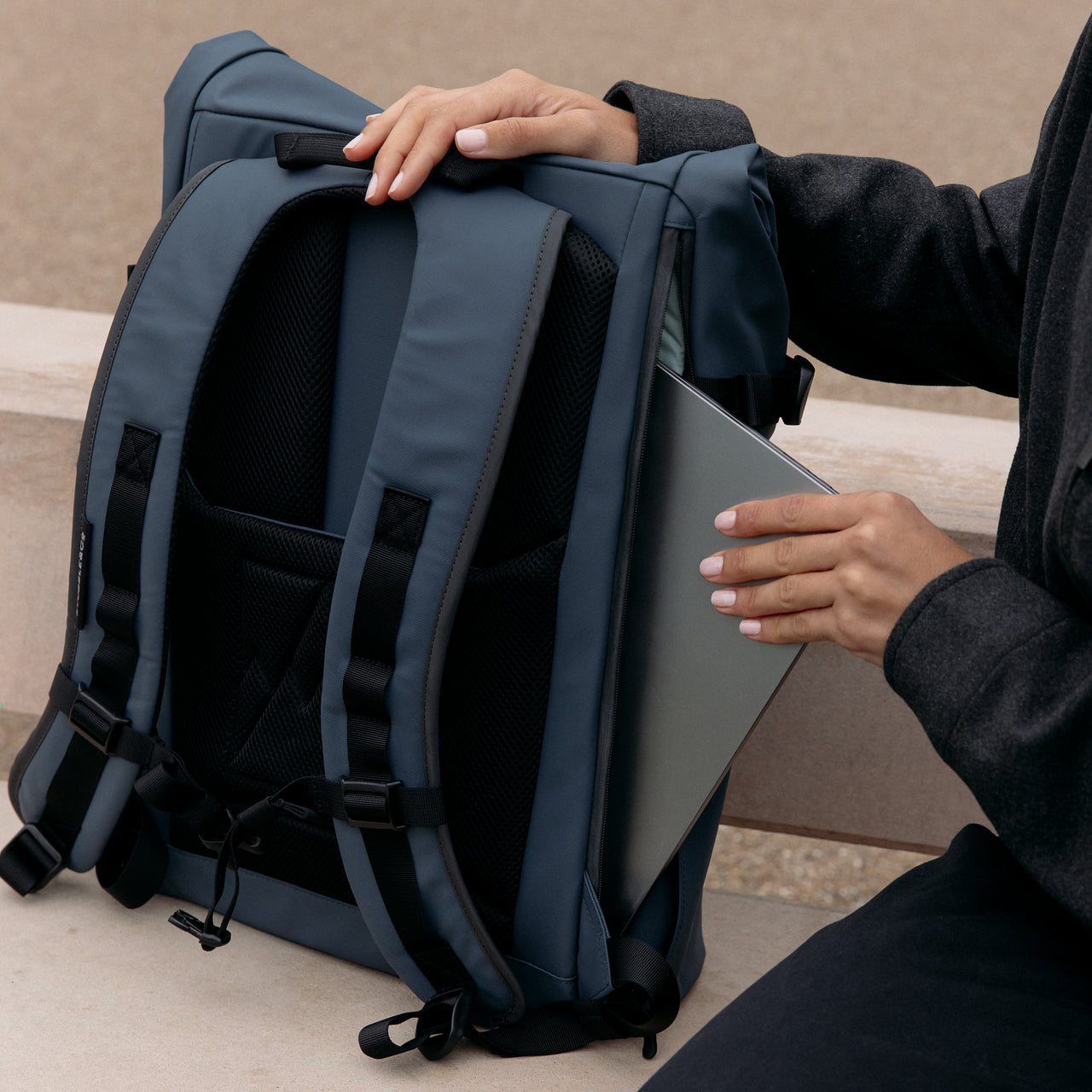 A woman placing a laptop into the secure and padded laptop compartment on the Roll Top 20L in Tasmin Blue