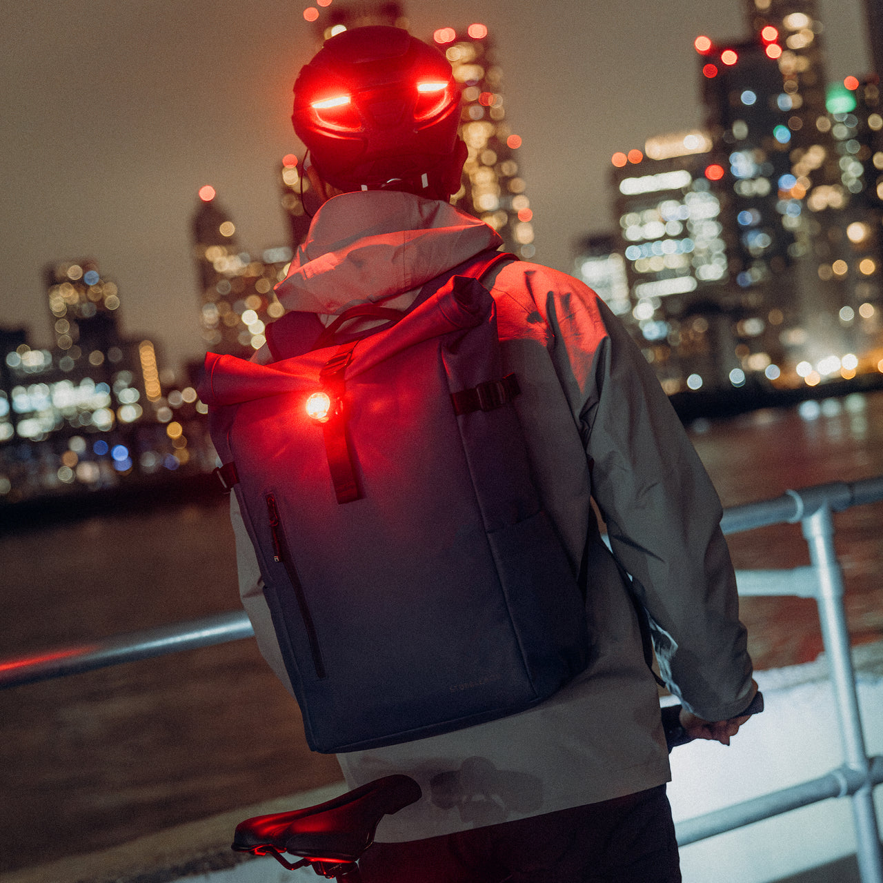A man on his bike looking over a river with his bike light attached to the Roll Top 20L backpacks on his back in Tasmin Blue
