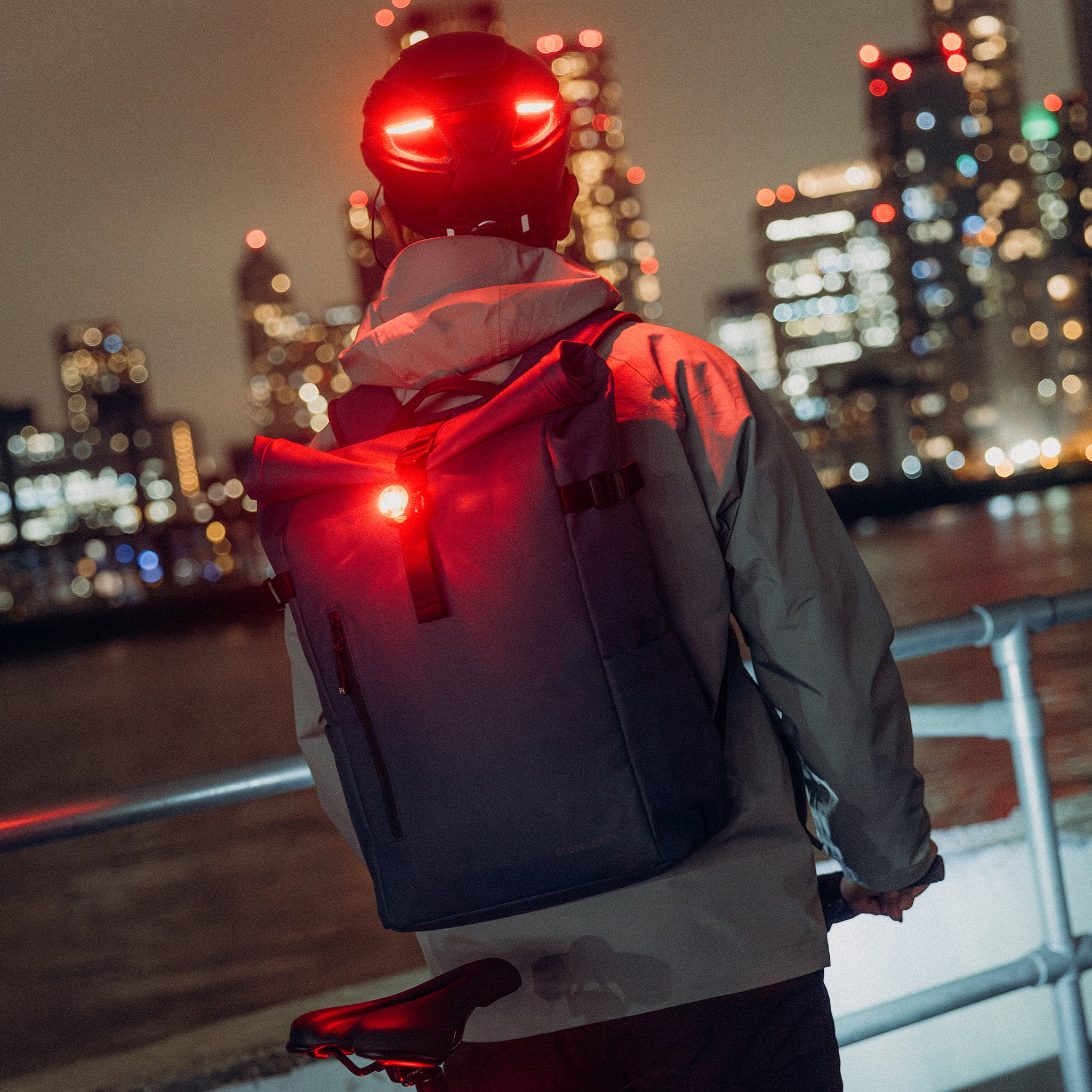 A man on his bike looking over a river with his bike light attached to the Roll Top 20L backpacks on his back in Tasmin Blue