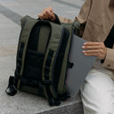 A woman placing a laptop into the secure laptop compartment on the Roll Top 15L backpack in Urban Green