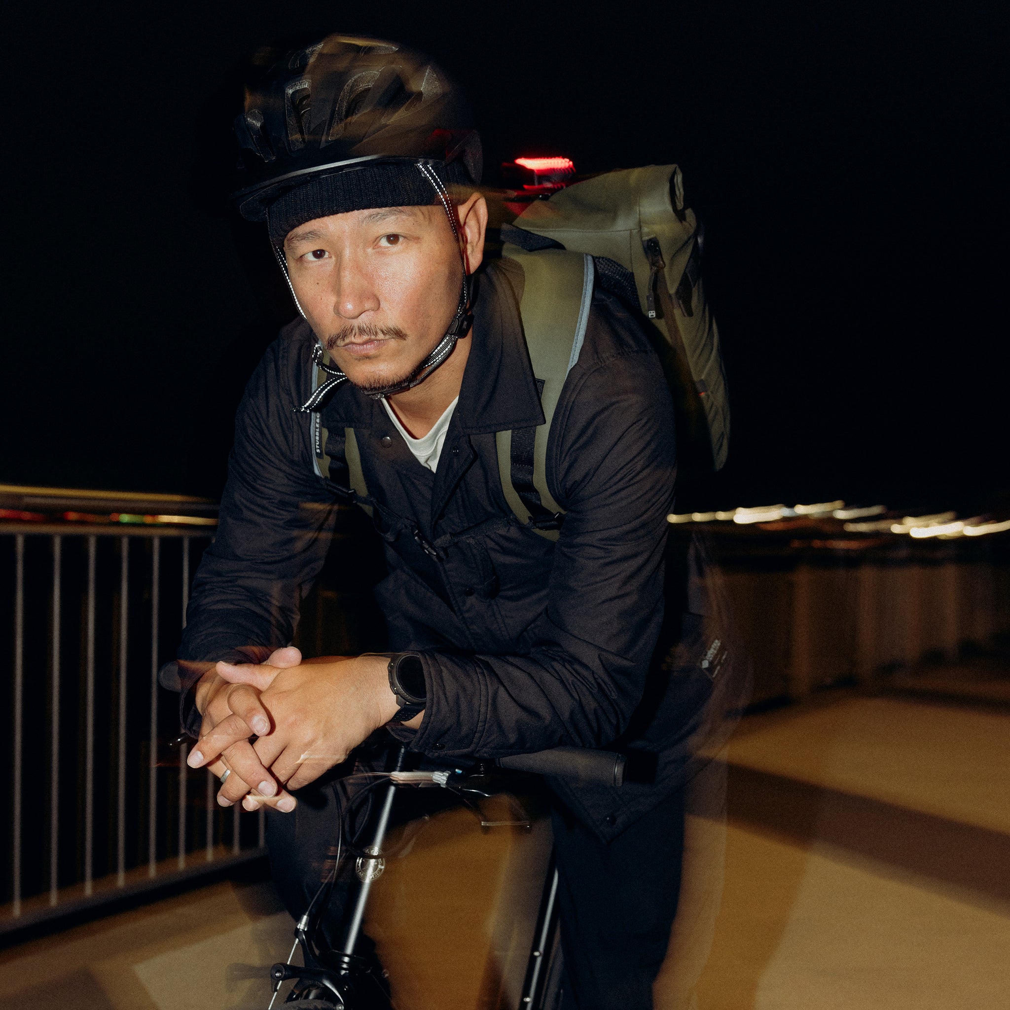 A man sitting on a bike wearing a Roll Top 20L backpacks in Urban Green on his back
