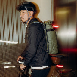 A man walking with his bike wearing a helmet and Urban Green Roll Top 20L backpack on his back