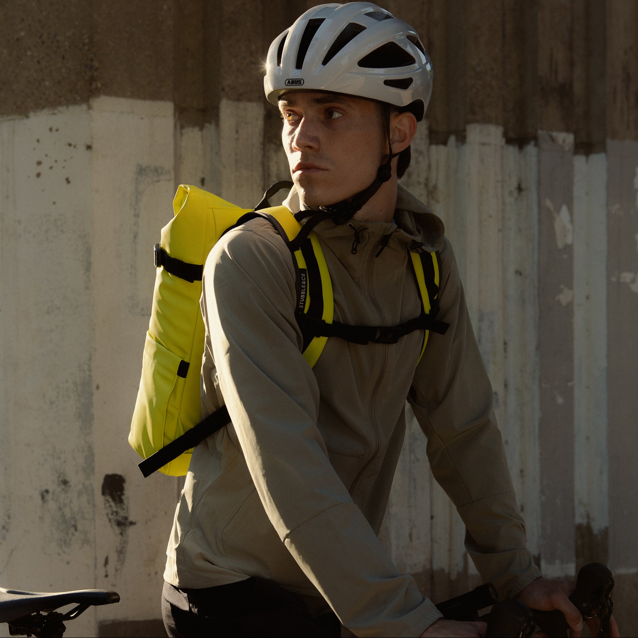A man sitting on a bike with a Roll Top 20L in Volt on his back with the chest straps done up