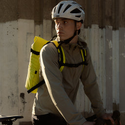 A man sitting on a bike with a Roll Top 20L in Volt on his back with the chest straps done up