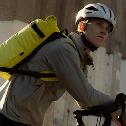 A man on a bike wearing a Roll Top 20L in Volt on his back with the chest straps done up