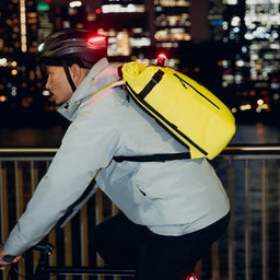 A man cycling along the river side with a Roll Top 20L Volt on his back