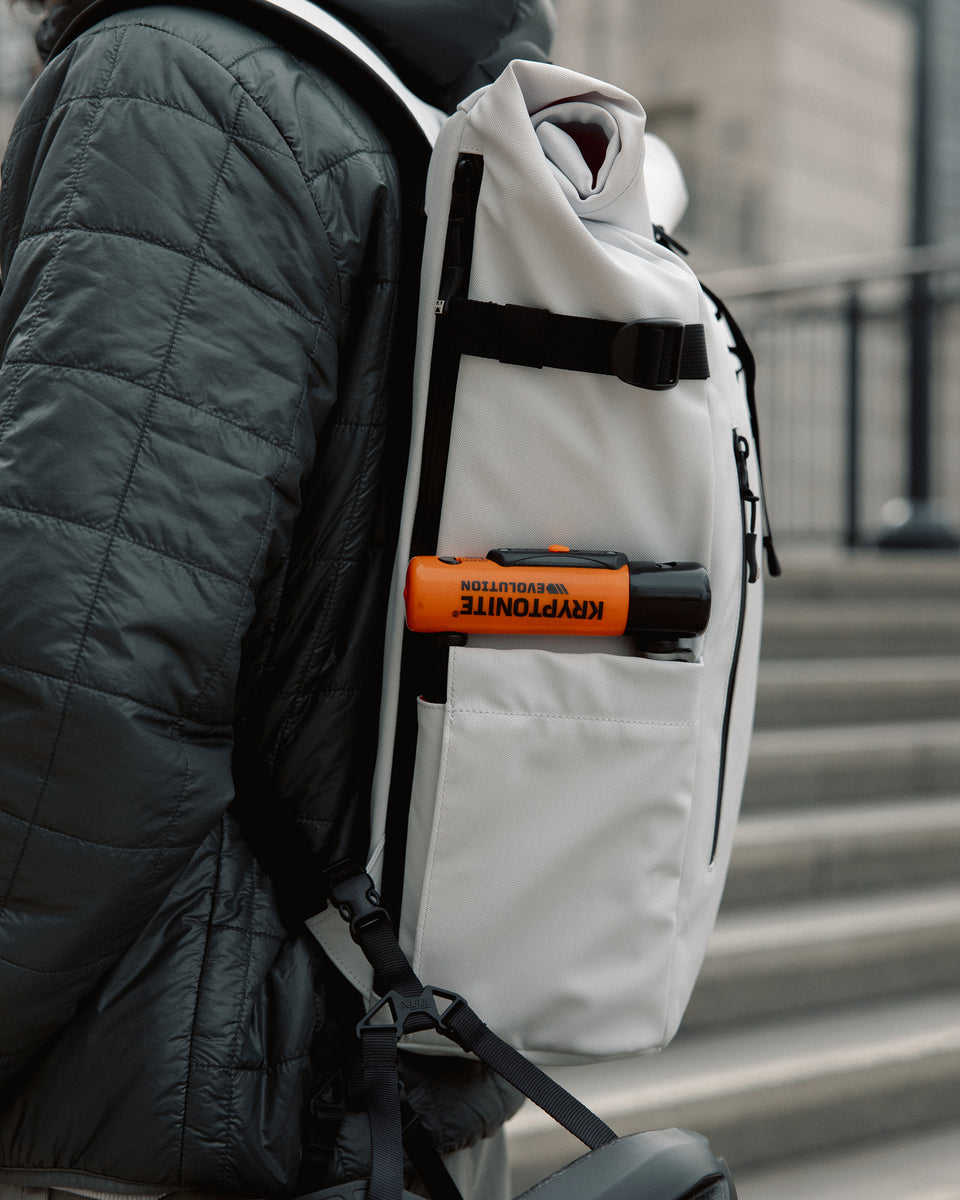 a close up of the side of an arctic white roll top 20l backpack with a bike lock in the side pocket