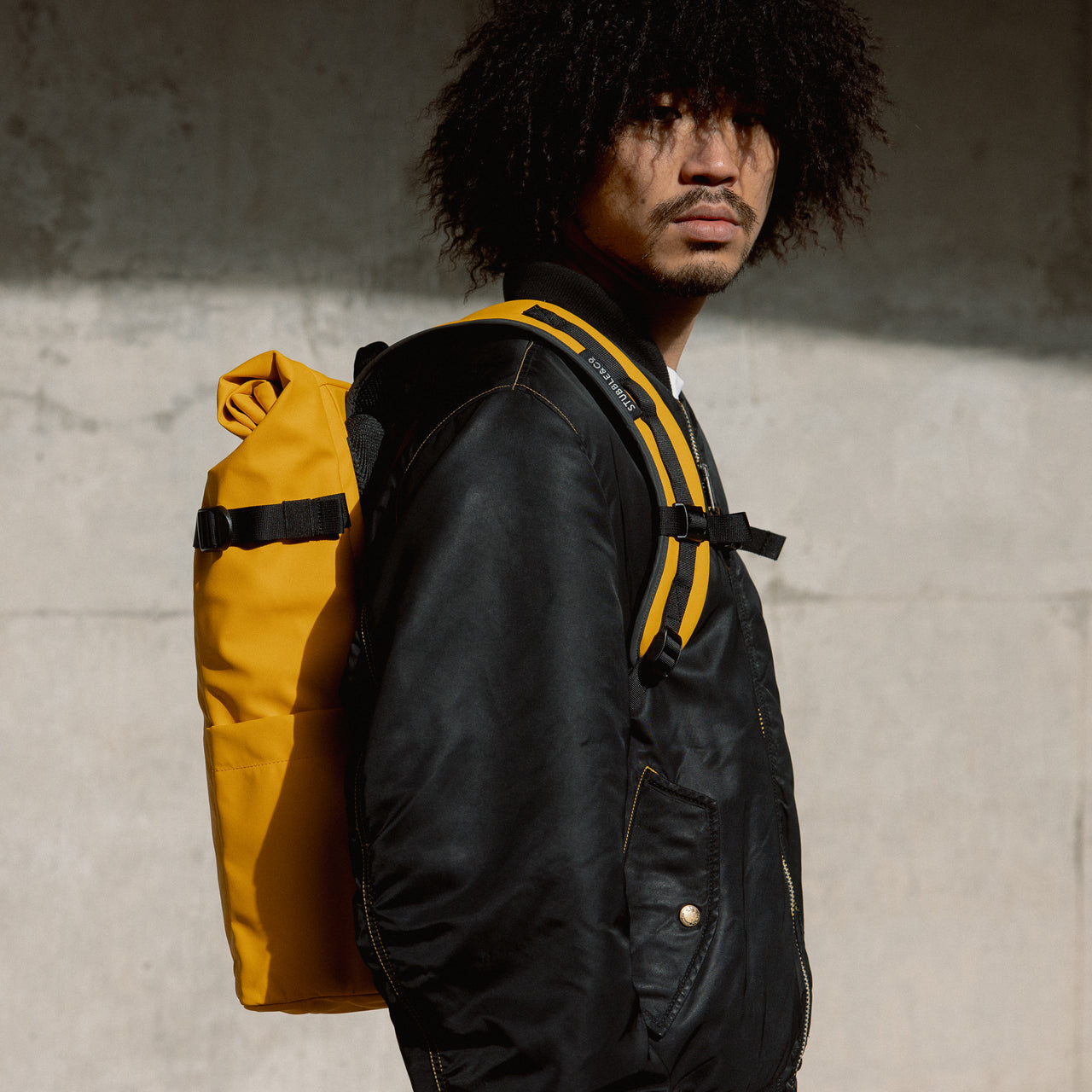A man staring into the camera whilst wearing a Yellow roll top 20l on her back