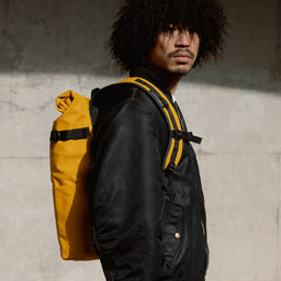 A man staring into the camera whilst wearing a Yellow roll top 20l on her back